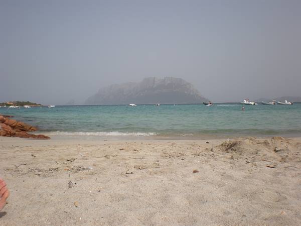 Pale sandy beach, boats on turquoise water, Tavolara island in the haze