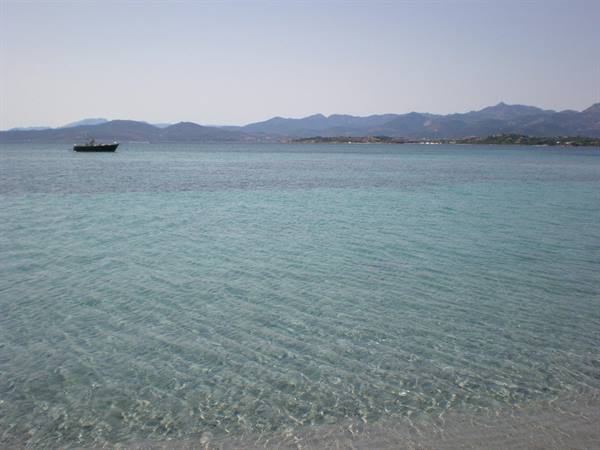 Clear turquoise water by the beach, fishing boat and mountains behind