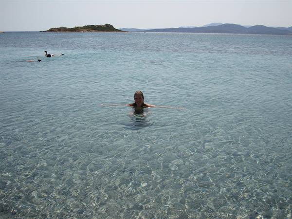 Woman swimming in clear turquoise water, islet and hills in the background