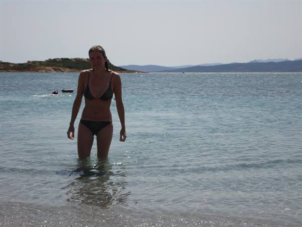 Woman in bikini wades through turquoise water in front of rocky islets