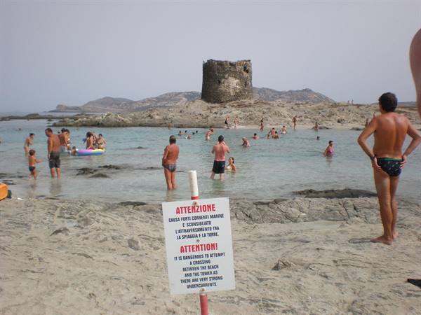 Swimmers in the cove beneath the ancient stone tower, warning sign in foreground