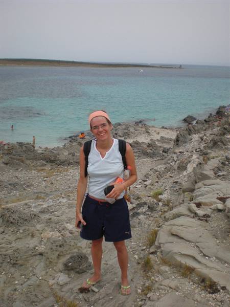Smiling woman with backpack on white rocks above turquoise sea