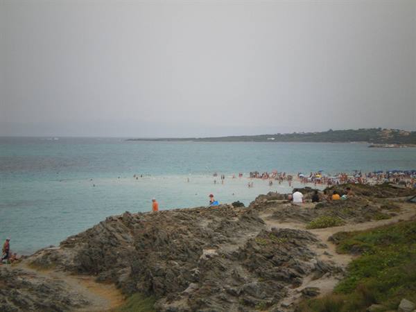 Swimmers on turquoise beach seen from granite rocks, overcast sky