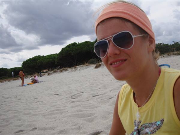 Girl with orange headband and sunglasses smiling on the sand, cloudy sky