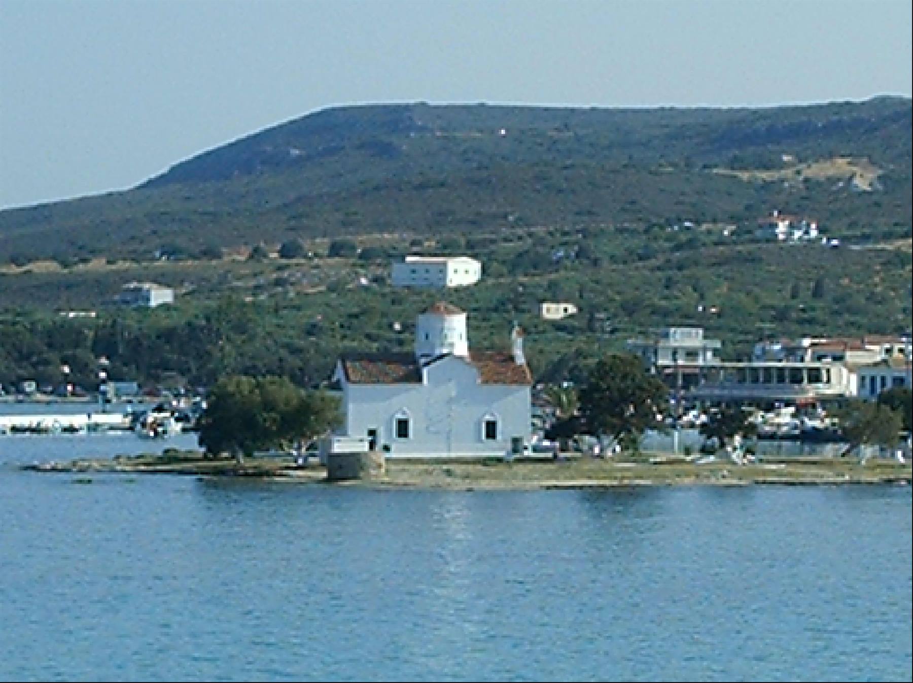 Small white domed church on an islet, harbor and green hills behind