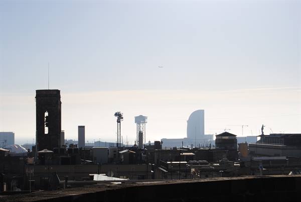 Barcelona skyline in the haze: bell tower, towers and Vela hotel against the sky