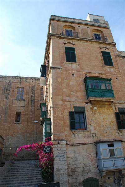 Golden limestone building with green balcony, stairs and bougainvillea, Valletta