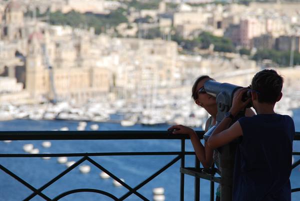 Two kids watch the harbor through a coin-operated binocular from a terrace