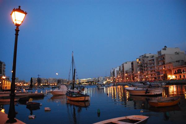 Lit lamppost on the quay, boats moored at Sliema harbor with illuminated buildings