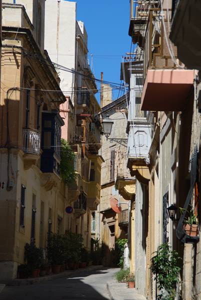 Narrow stone alley with traditional wooden balconies and potted plants, Malta