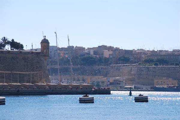 Stone watchtower on harbour walls, small boats float on sunlit water