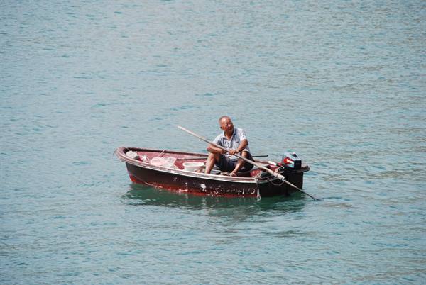 Fisherman rowing an old red wooden boat on teal water