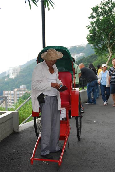 man in straw hat beside a red rickshaw at Victoria Peak