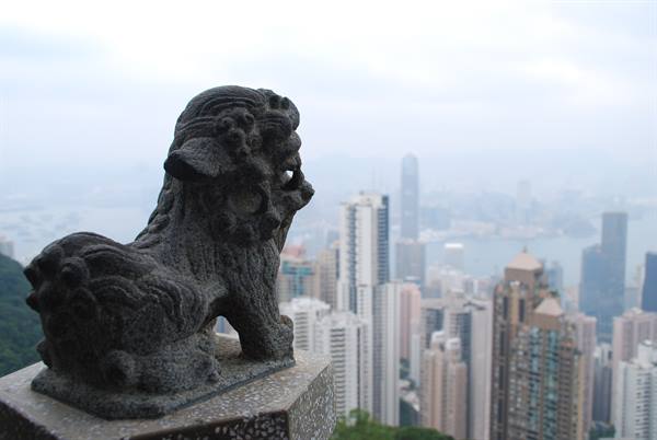 Stone lion statue at Victoria Peak overlooks misty skyscrapers of Hong Kong