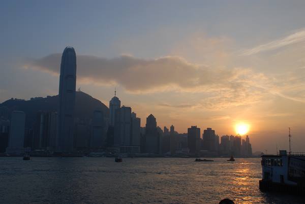 Hong Kong skyscrapers silhouetted against the low sun over the harbour, boats on water