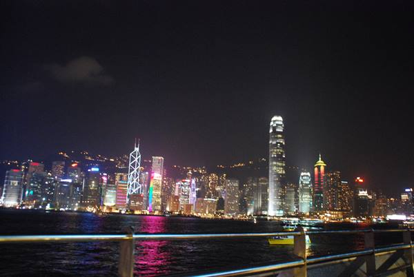 Hong Kong illuminated skyscrapers reflected in the harbour at night, railing in foreground