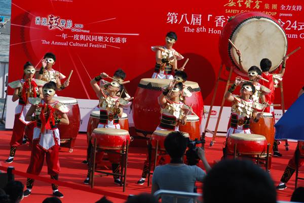 Children in painted masks playing red drums at Hong Kong cultural festival