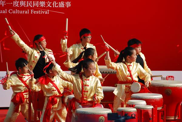 Children in yellow and red costumes play traditional drums at cultural festival