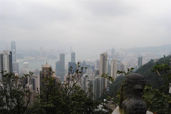 Skyscrapers over the hazy bay from Victoria Peak, stone lion statue in foreground