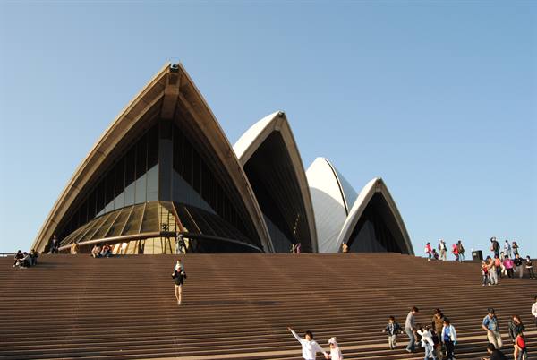 Turisti sulla grande scalinata dell'Opera House di Sydney sotto cielo azzurro