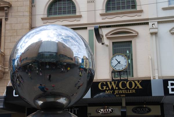 La grande sfera specchiata di Rundle Mall riflette la folla davanti all'orologio di G.W. Cox, Adelai