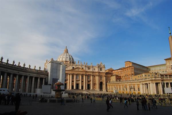 St. Peter's Square in Rome with the basilica, colonnade and tourists under a blue sky