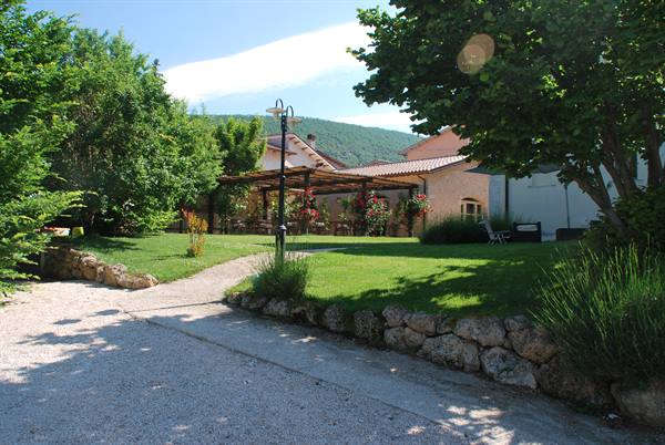 Green garden with gravel path, stone wall and rose-covered pergola under blue sky