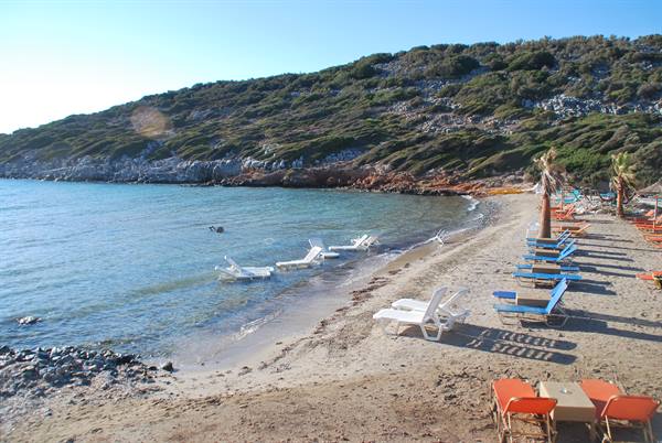 Empty sun loungers on sand and in water, green hill behind