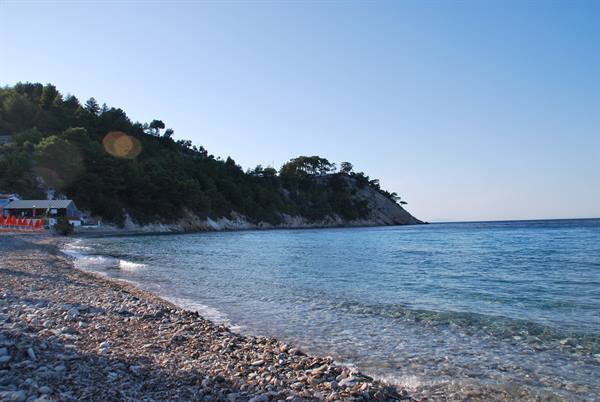 Pebble beach with red umbrellas and clear sea beneath a green hill
