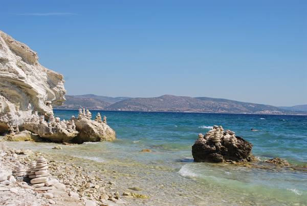 Balanced white pebbles stacked on rocks by clear turquoise sea, white cliffs nearby