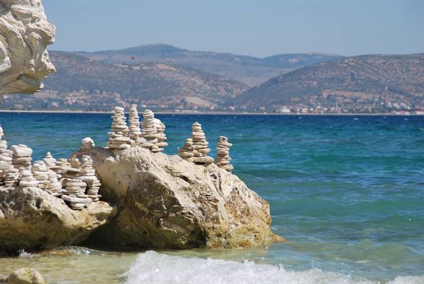 White pebbles stacked on a rock by turquoise sea, dry hills behind