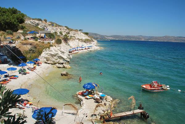 Pebble beach with blue umbrellas, anchored red boat and white rocky cliff