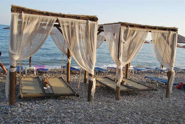 Wooden cabanas with white curtains on pebble beach by the sea