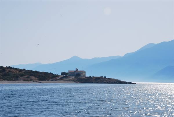 Small bell-towered house on rocky headland, hazy blue mountains behind