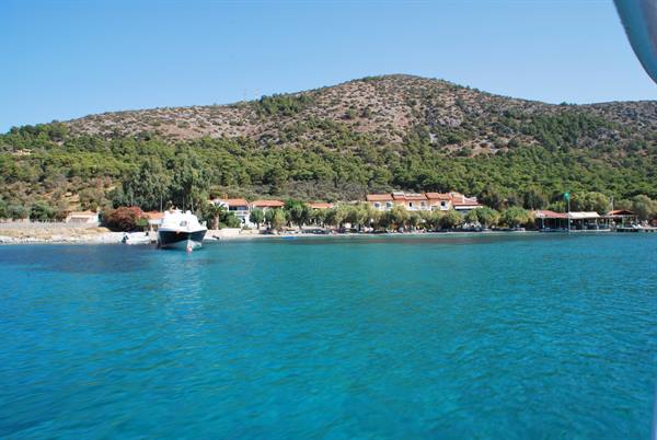 White boat anchored off a beach with houses, turquoise water and green hill