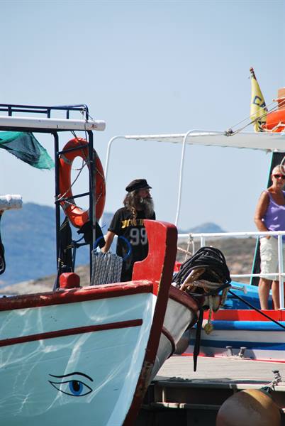 Bearded fisherman on white boat with painted eye, Greek harbor