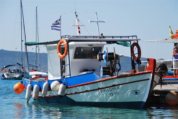 White and blue fishing boat moored at the dock, Greek flag and orange buoys