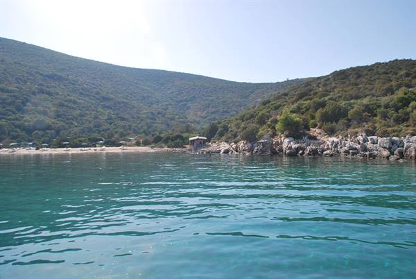 Turquoise water in front of sandy beach and green hills with umbrellas