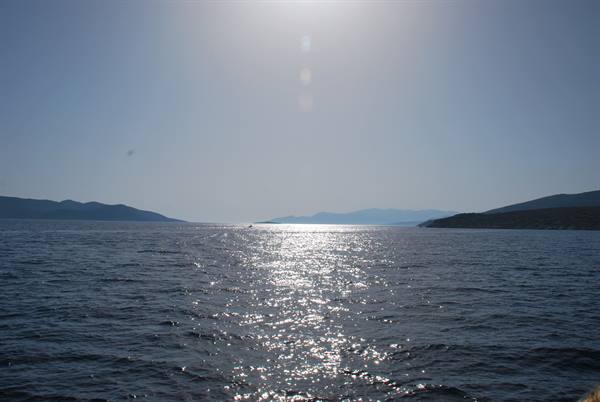 High sun over the sea, sparkling reflections on water between dark hills