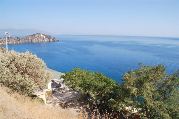 House among trees above a blue bay, a windmill on the rocky point
