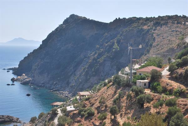 houses and a small wind turbine on the green hillside above the rocky bay