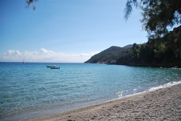 White boat on pebble beach, blue sea and sunny green hillside