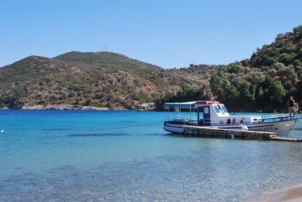 White and blue excursion boat moored at wooden pier, turquoise water and green hills