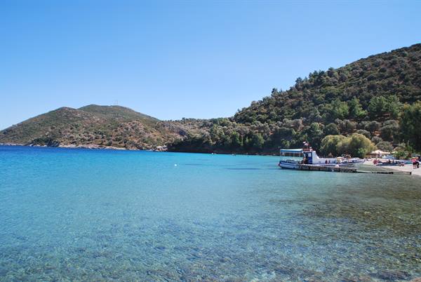 Tour boat moored at the beach, clear turquoise water, green hills