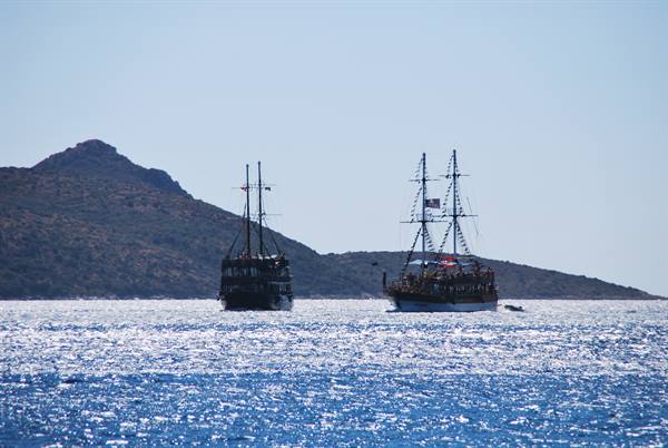 Two tourist sailing ships cruise sparkling sea in front of dry hills