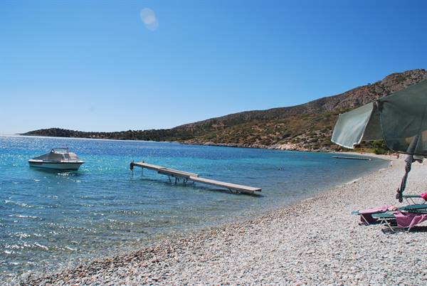 Boat moored near the wooden pier on the pebble beach with parasol