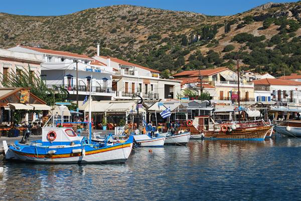 Colorful fishing boats in Batsi harbor, whitewashed houses and dry hills behind