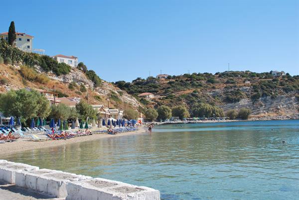 Sandy beach with blue umbrellas, tavernas and houses on the hill