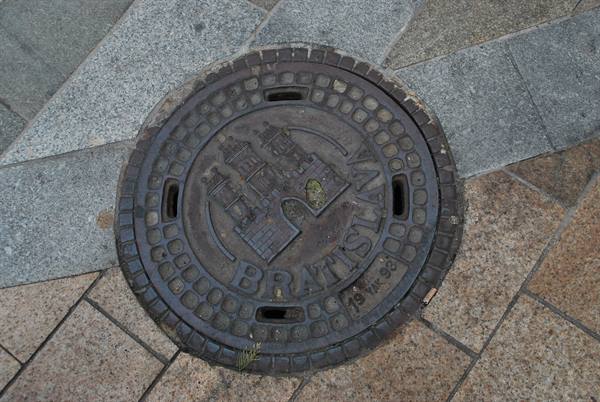 Cast iron manhole cover with castle and Bratislav inscription embedded in pavement