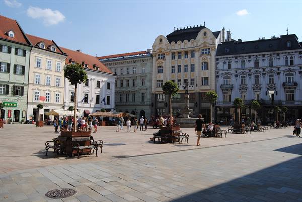 Bratislava main square, historic buildings, pedestrians, benches and planters under sunny sky